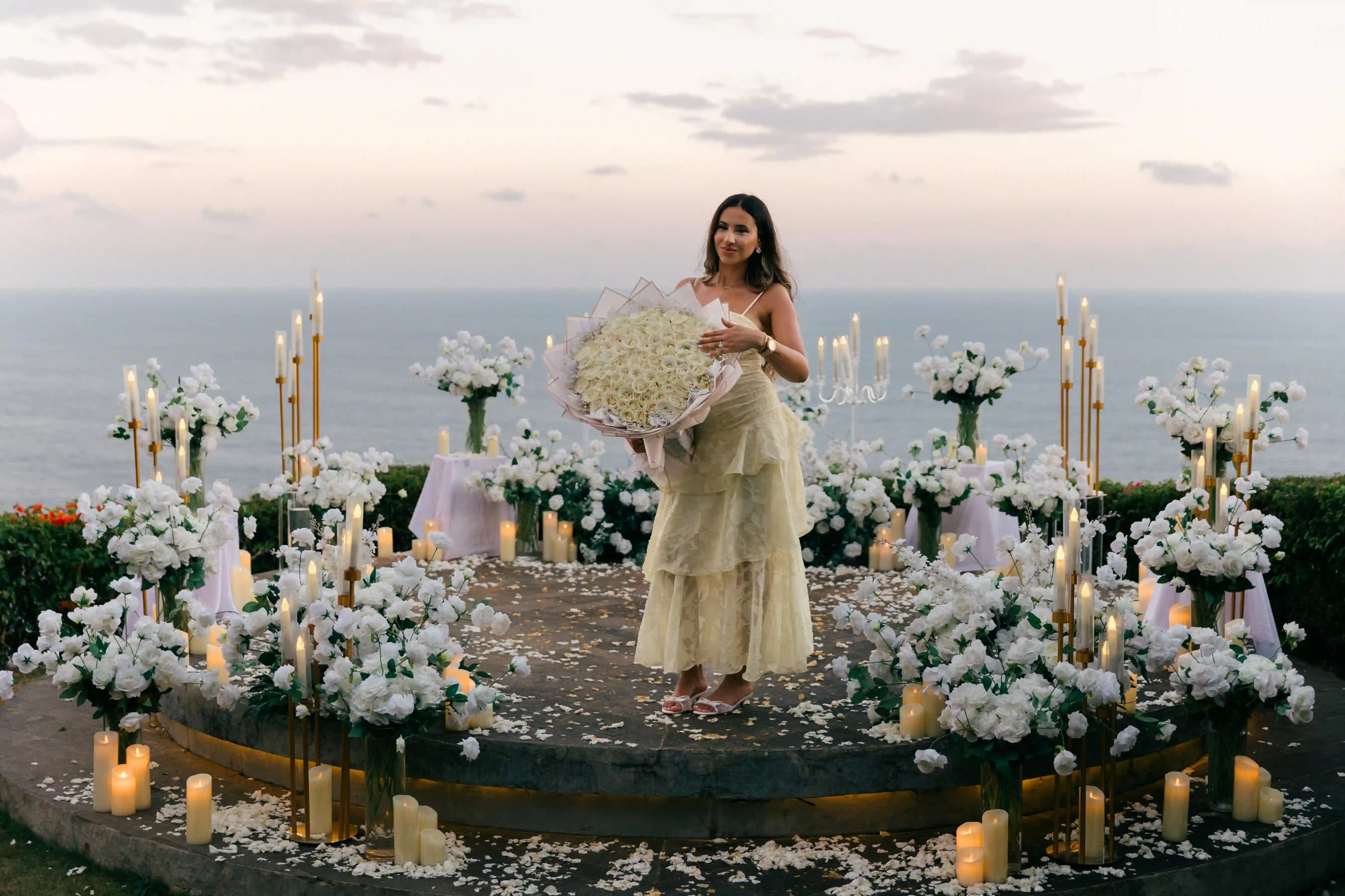 Bride holding a white bouquet at a cliff proposal setup in Bali