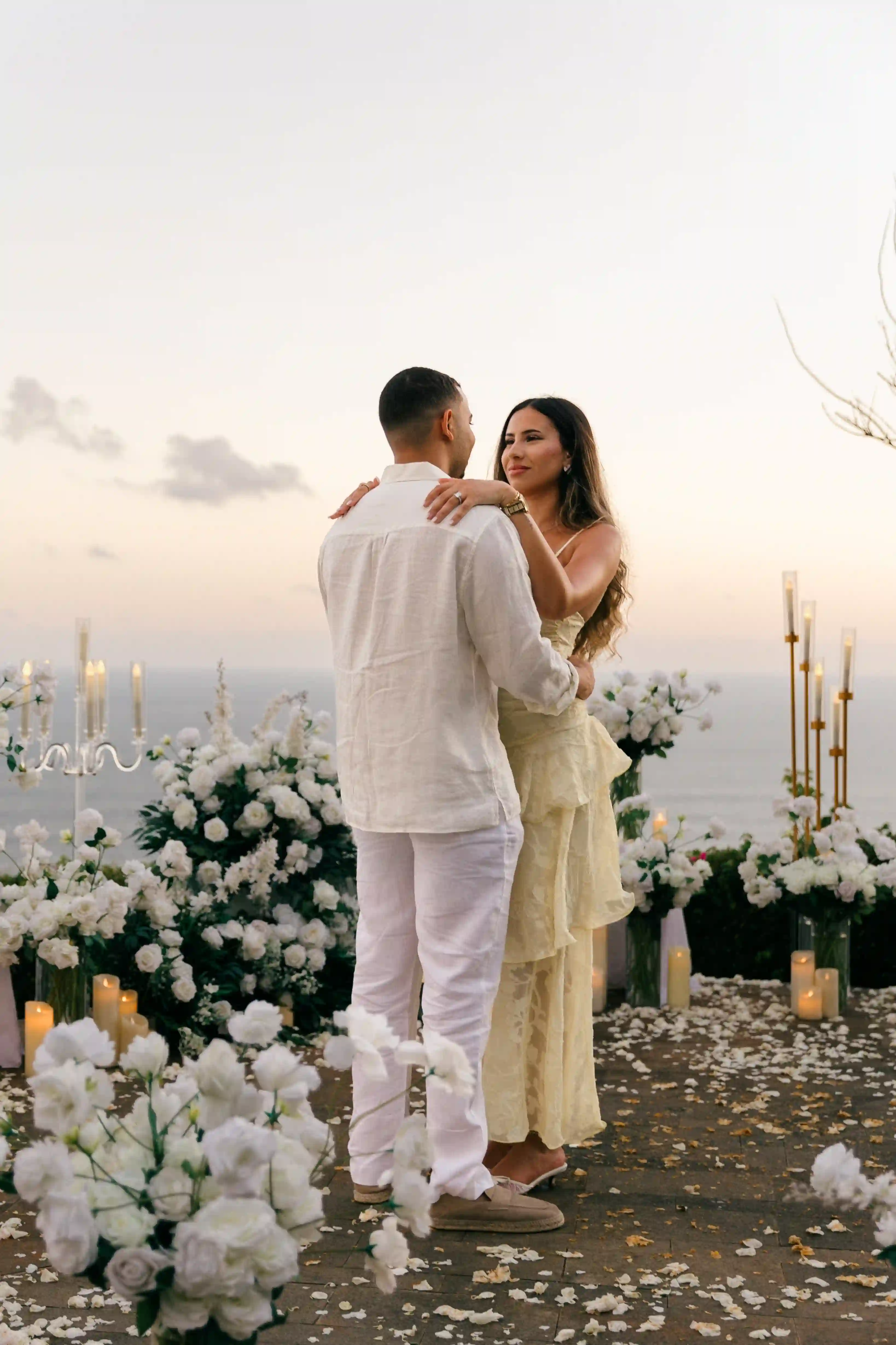 Couple embracing among white flowers at a Bali clifftop proposal