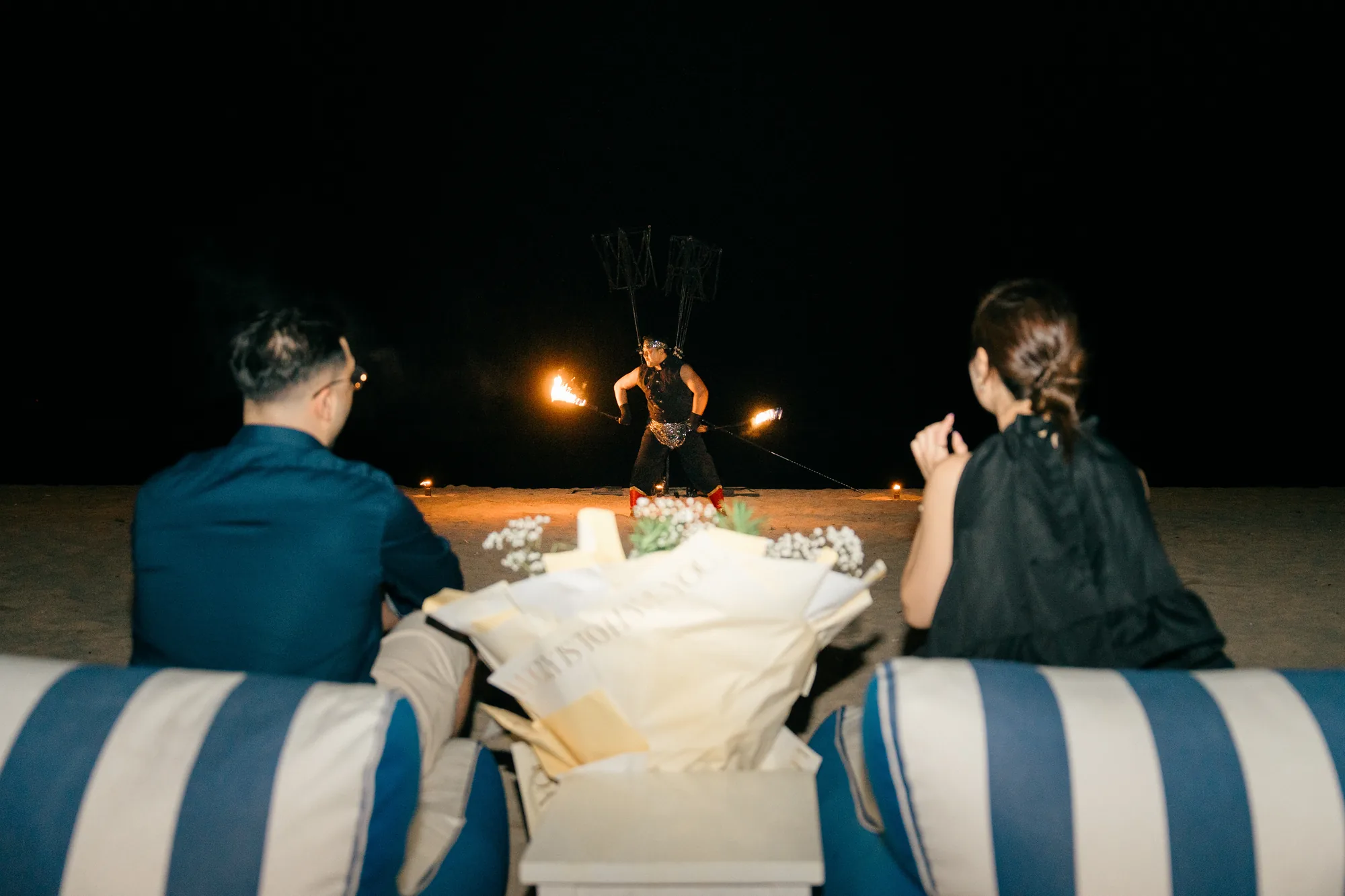 Couple watching a private fire show on the beach at night during a Bali proposal