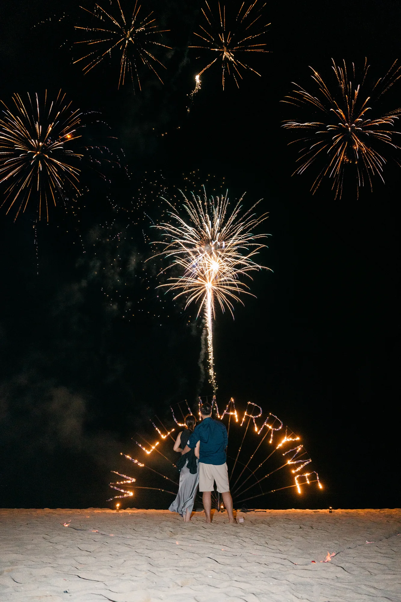 Couple beneath a bursting firework at their beach proposal in Bali