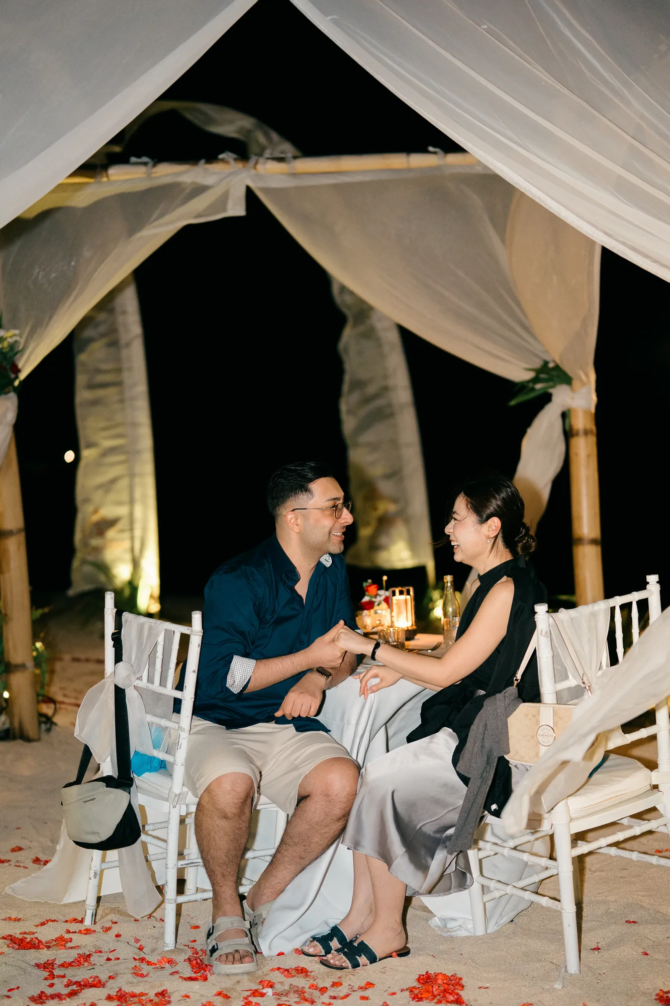 Couple at an intimate candlelit dinner in a draped beach cabana during their Bali proposal