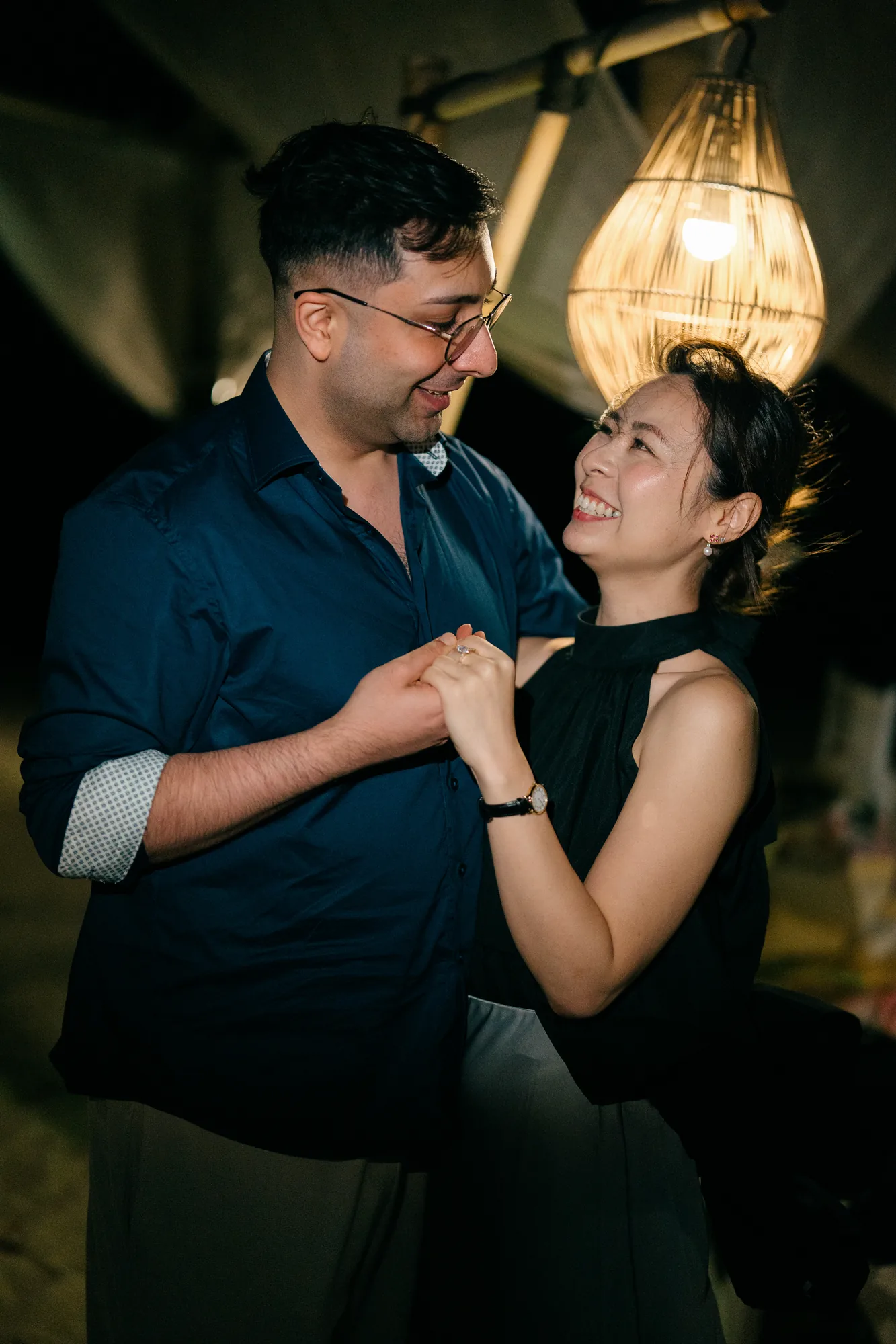 Couple embracing under a draped beach cabana with a chandelier at a Bali proposal