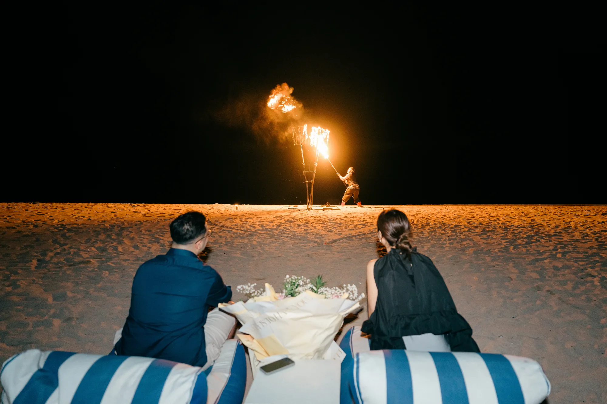 Couple watching a beach fire show from their dinner setup at a Bali proposal