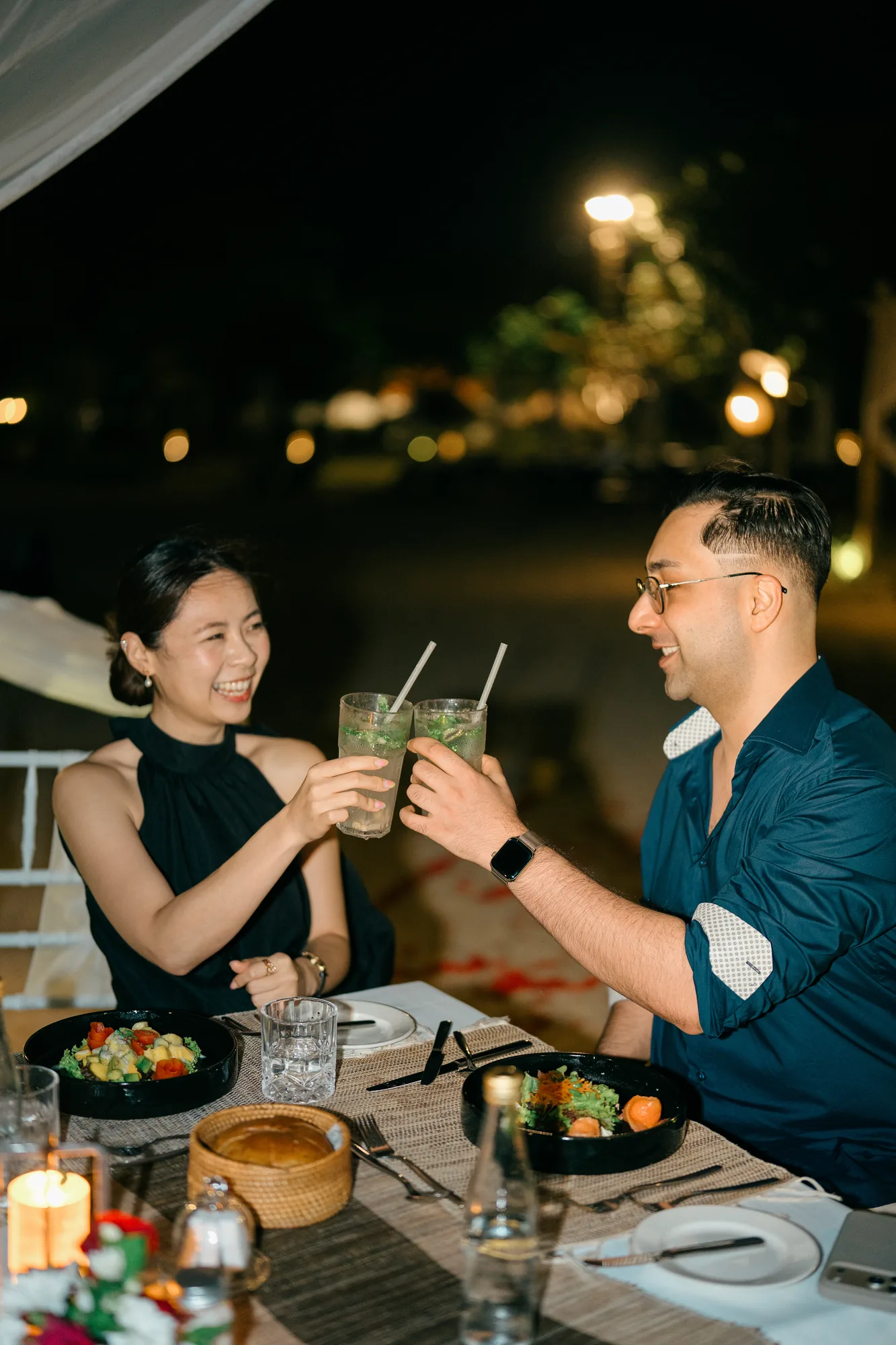 Couple toasting cocktails at a candlelit beach dinner during their Bali proposal
