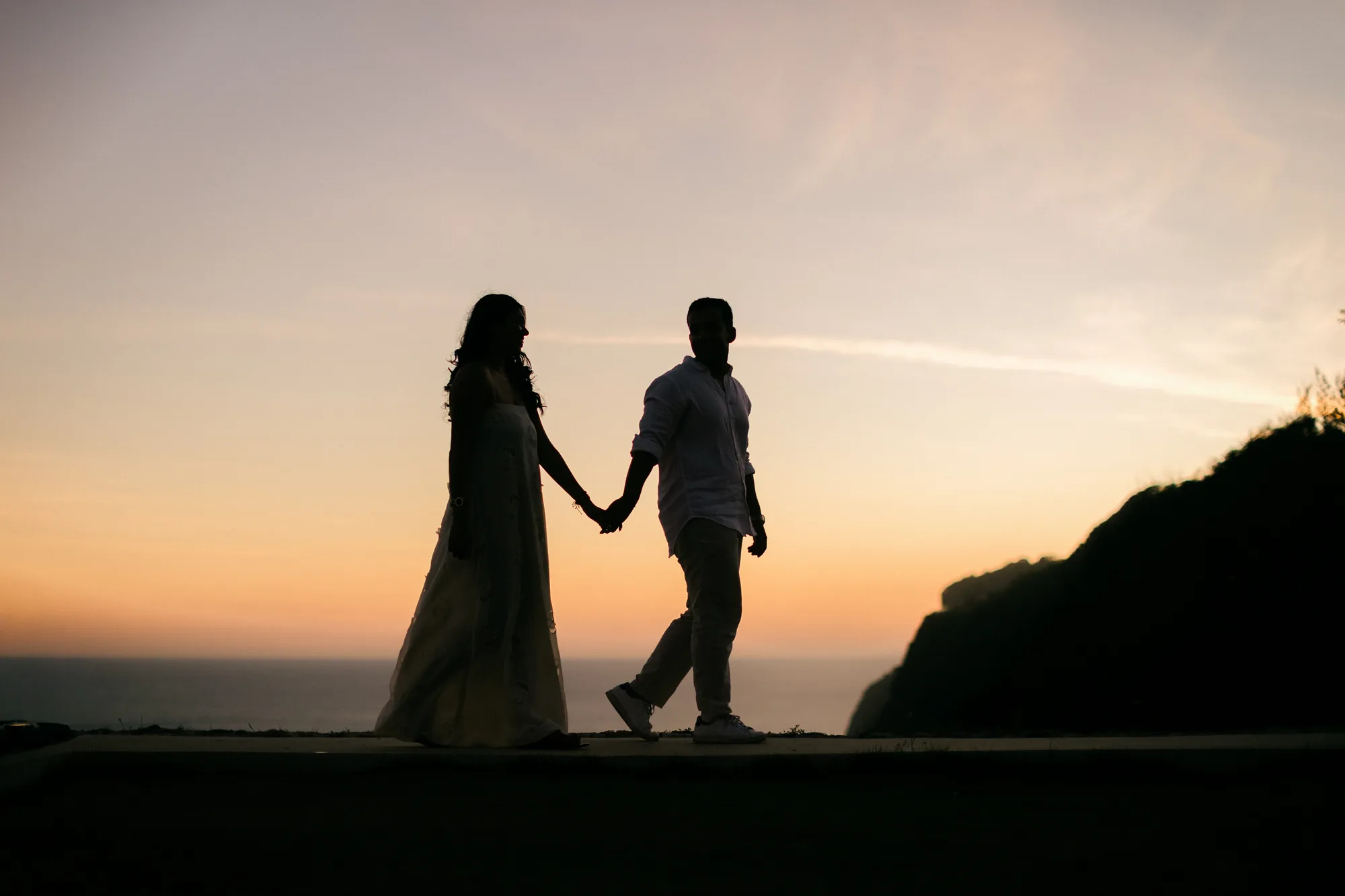 Couple silhouetted holding hands against the sunset during a Bali cliff proposal