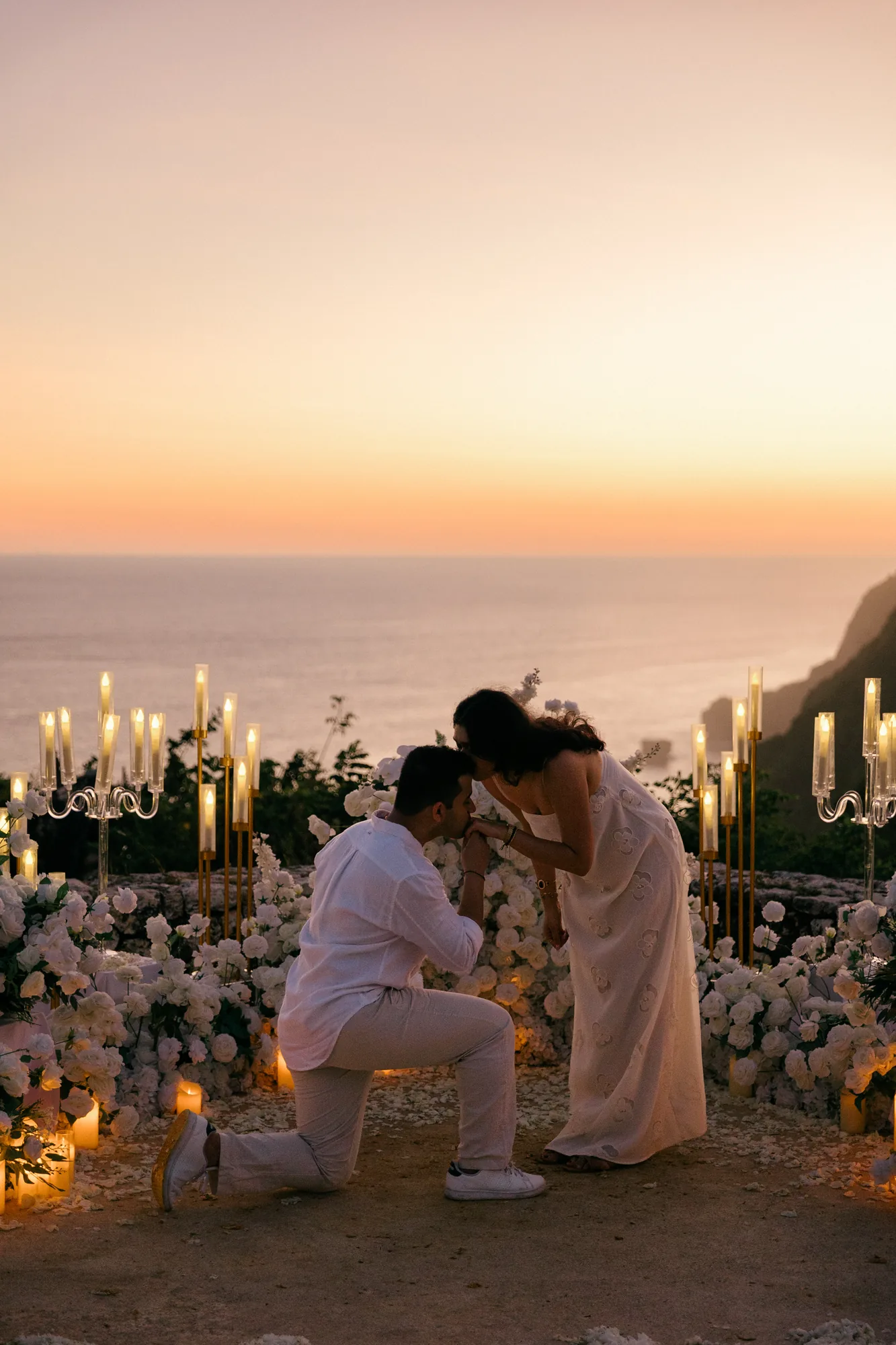 Man kneeling to propose at a candlelit clifftop setup at sunset in Bali