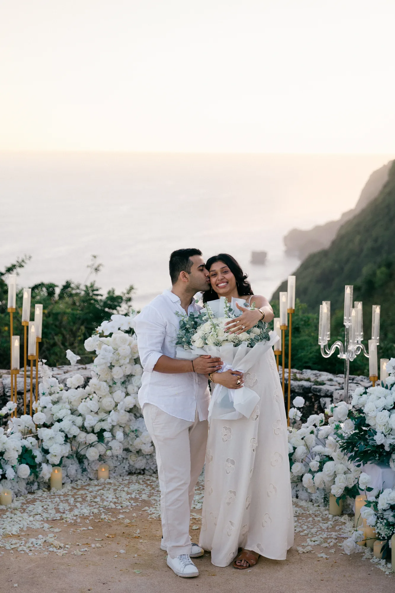 Couple kissing at their clifftop floral proposal setup at sunset in Bali