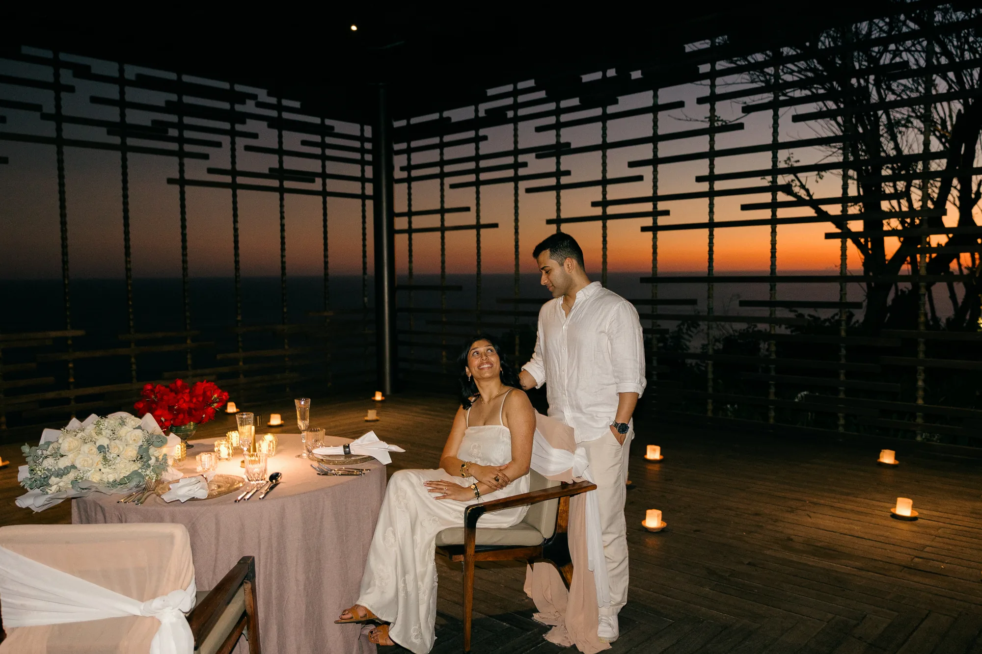Couple at a private dinner table in a cliffside pavilion at sunset during a Bali proposal