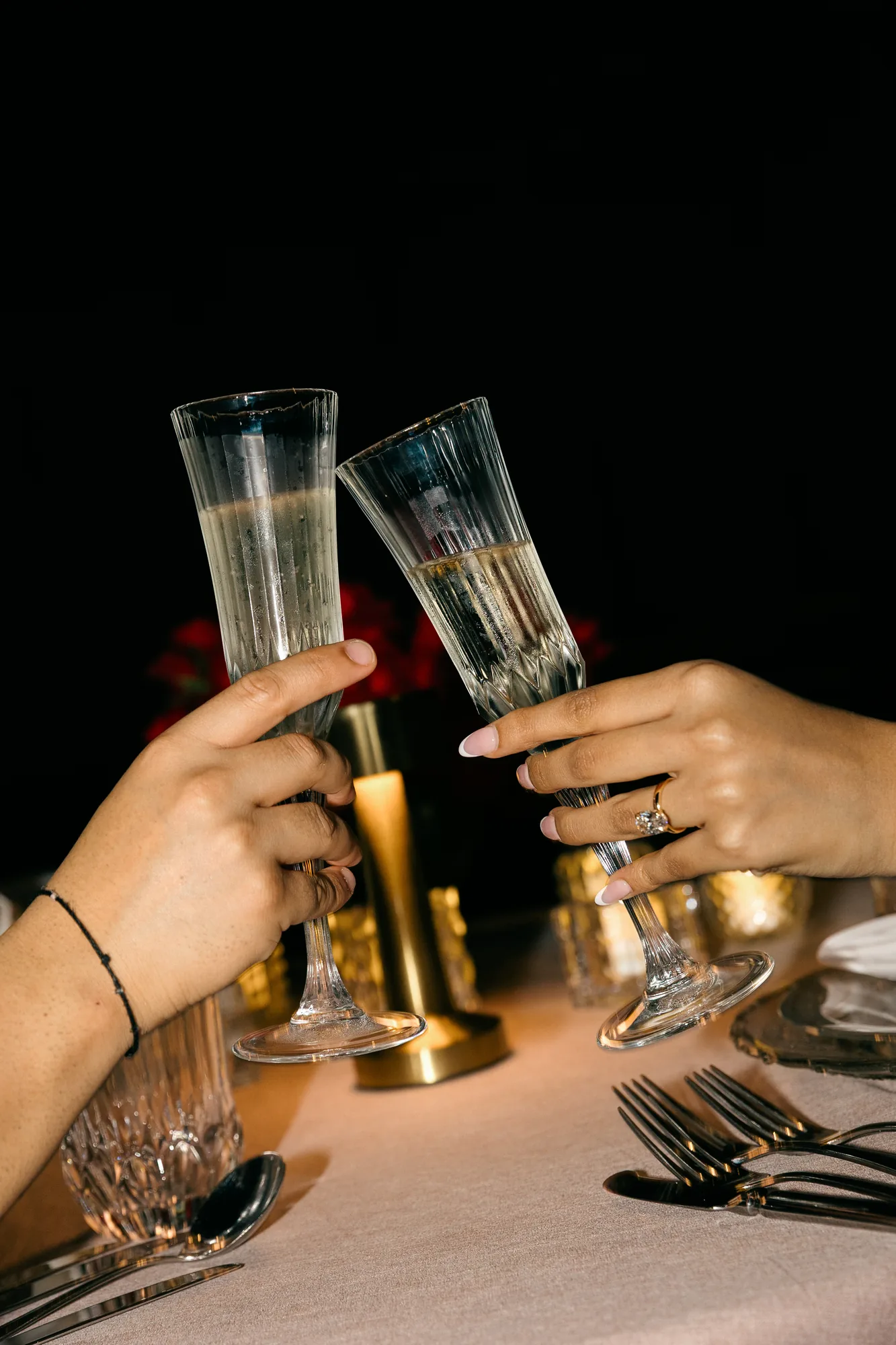 Two champagne glasses raised in a toast at a candlelit dinner during a Bali cliff proposal