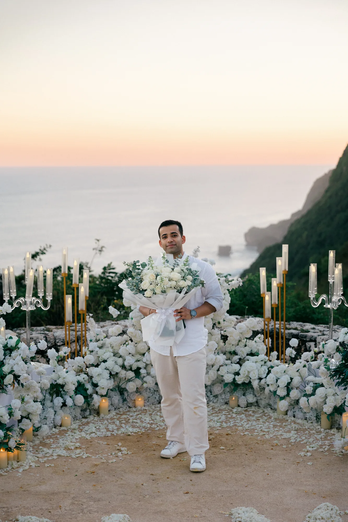 Man holding a white bouquet at the clifftop floral proposal setup in Bali