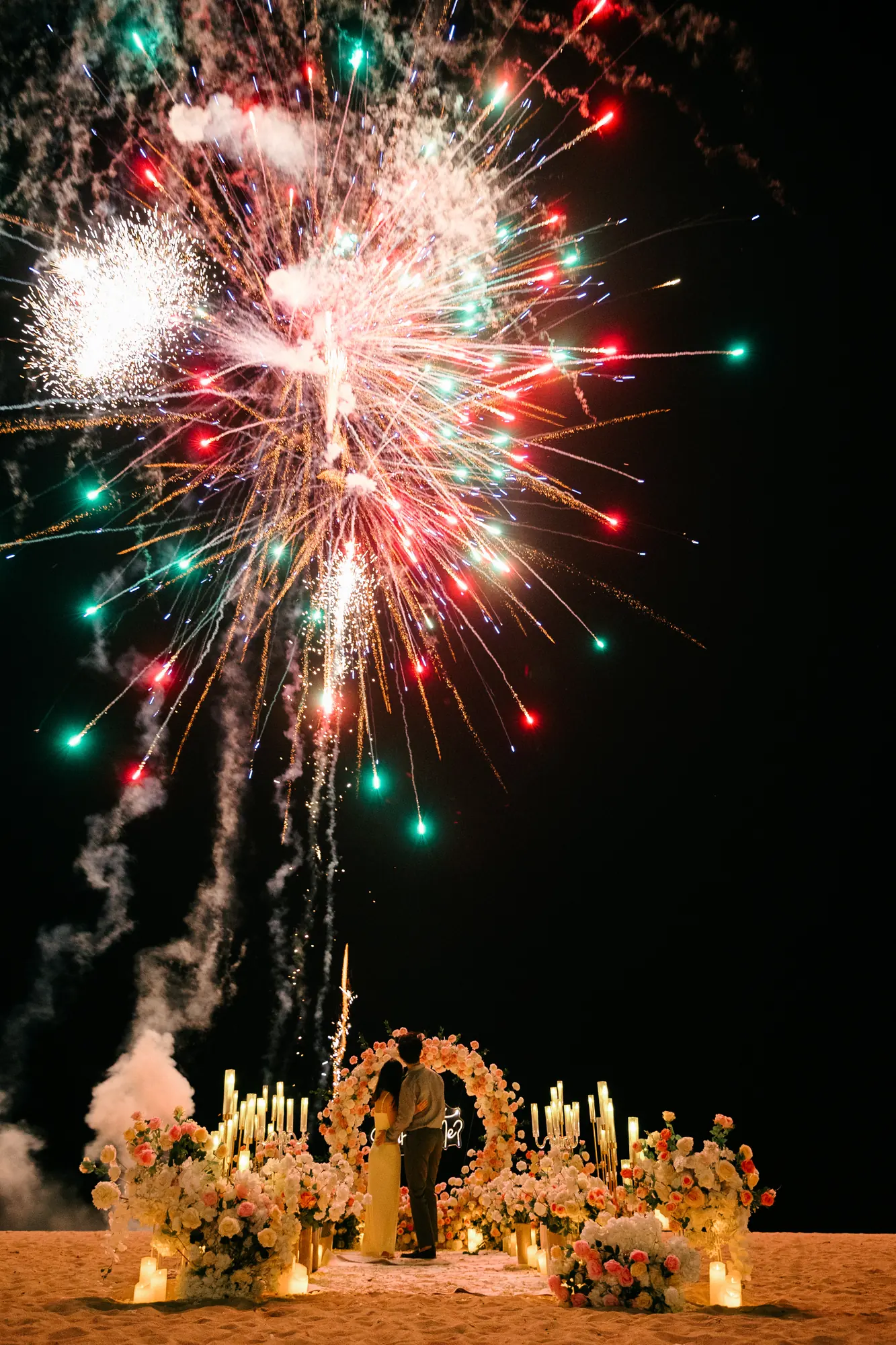Colourful fireworks over a floral arch at a Bali beach proposal