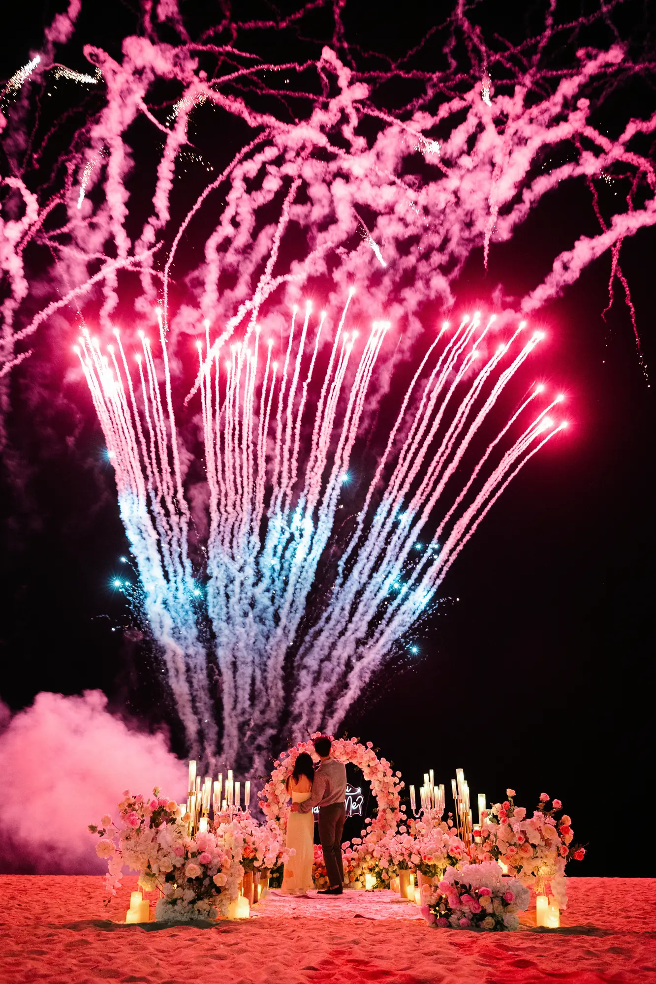 Pink fireworks and coloured smoke over a floral arch at a Bali beach proposal