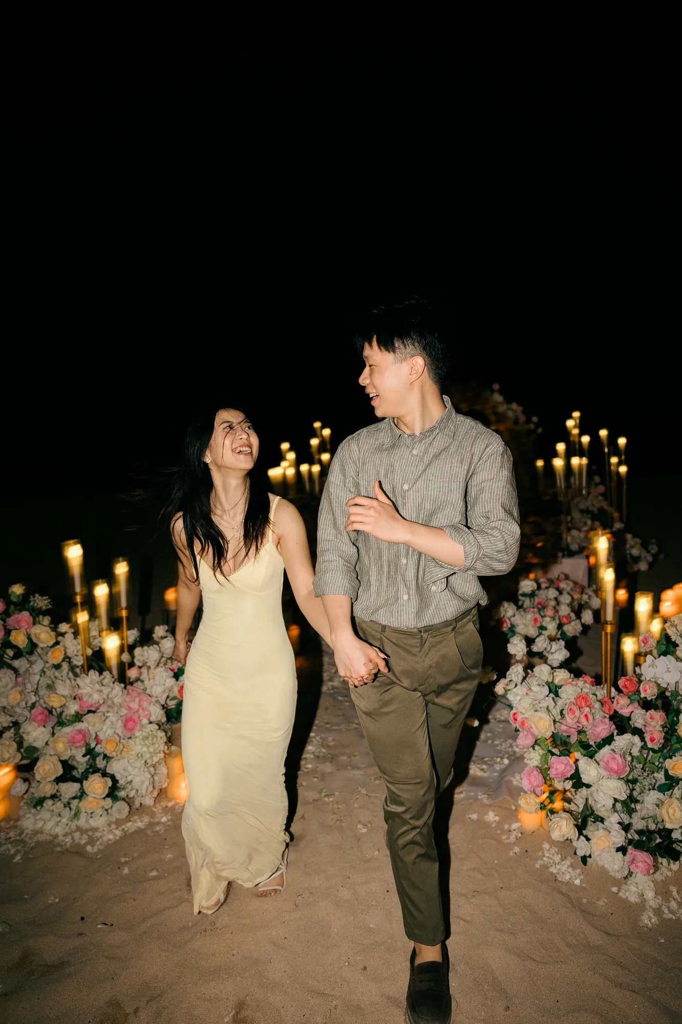 Couple walking hand in hand past candlelight at their Bali beach proposal
