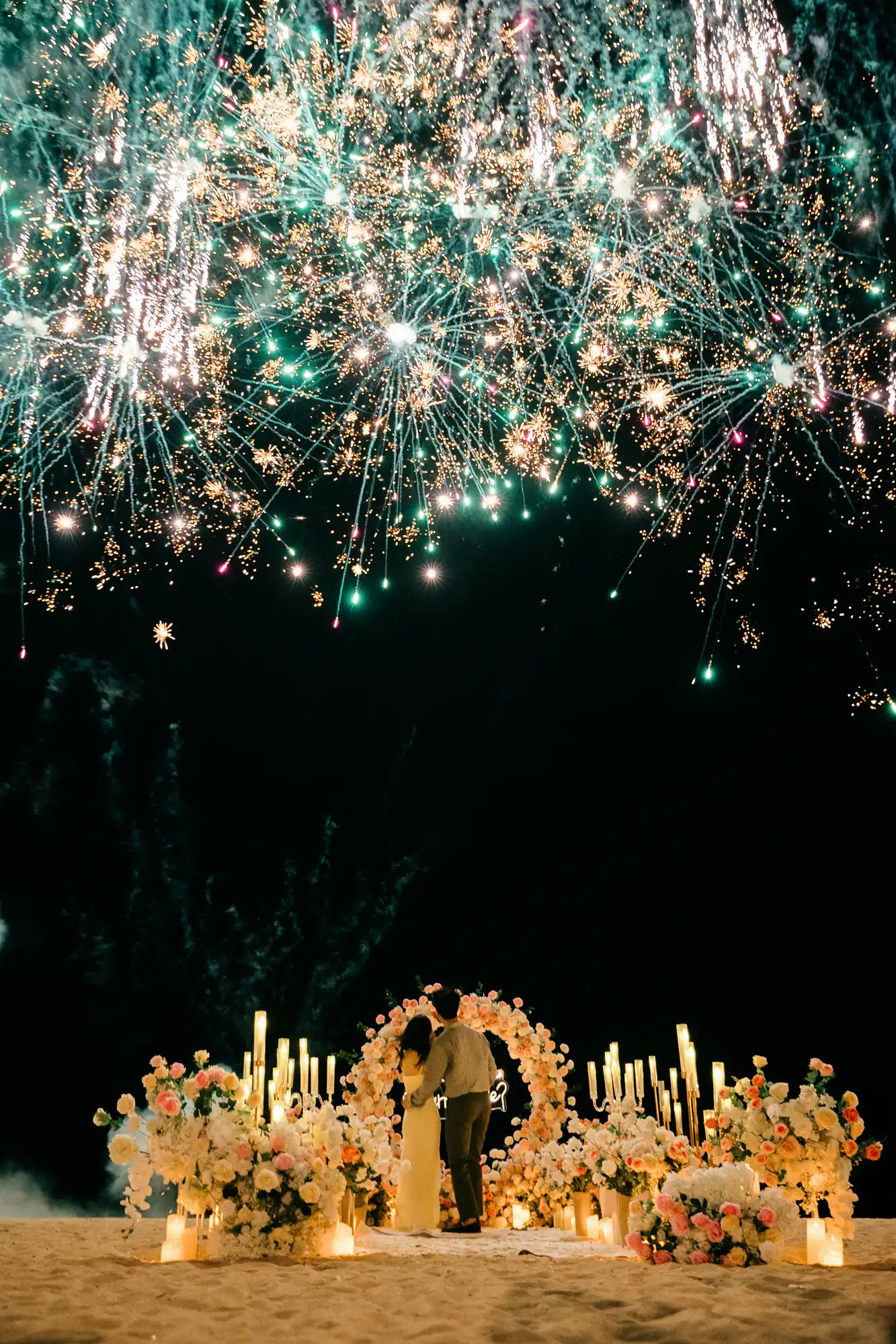 Teal and white fireworks over a beach proposal setup in Bali