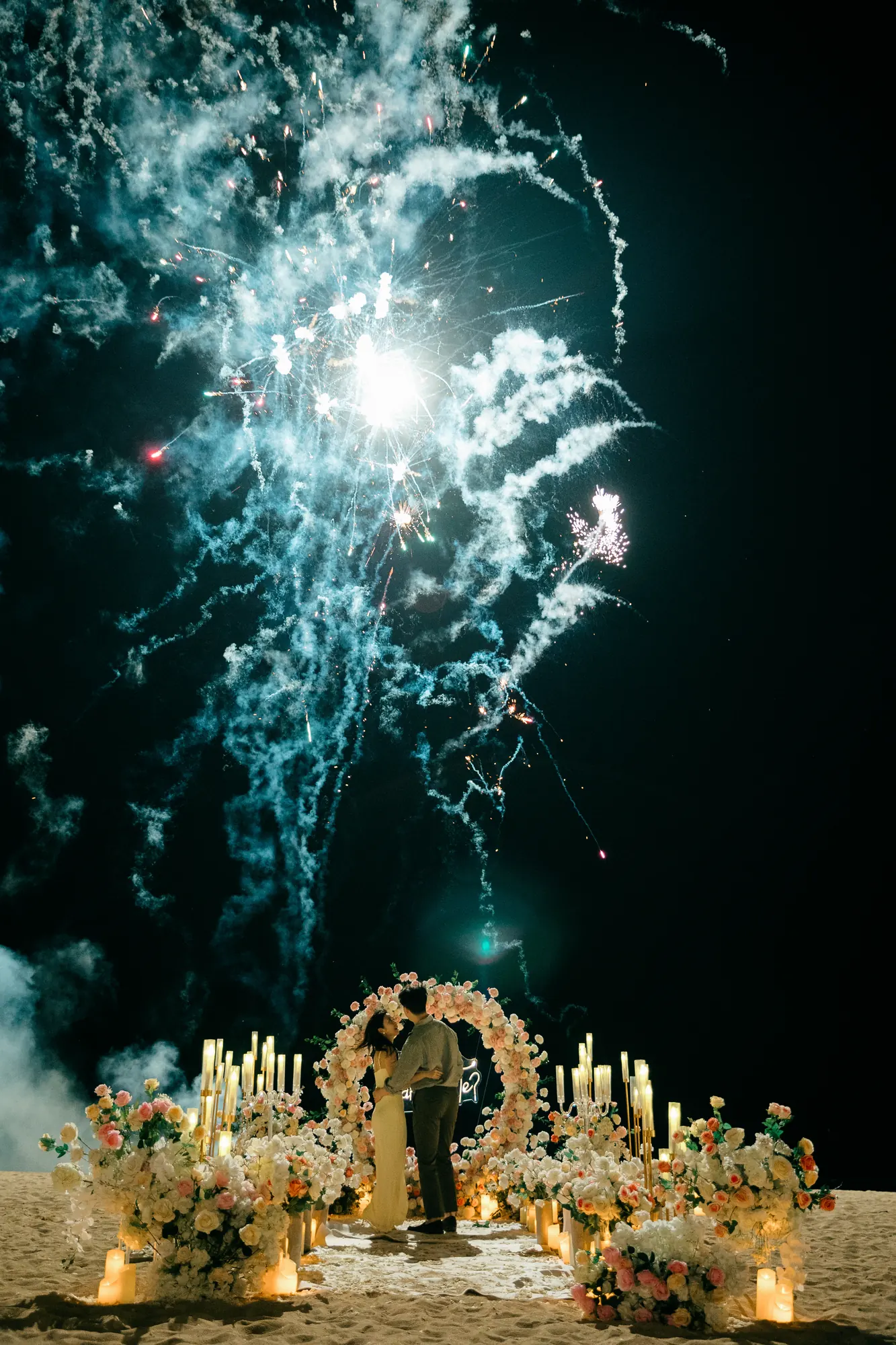 Fireworks bursting over a floral arch at a Bali beach proposal at night