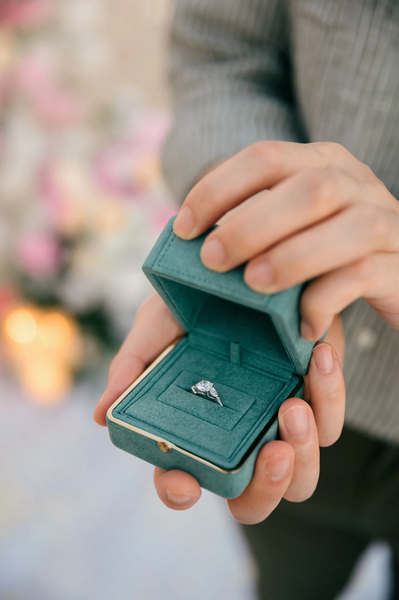 Hand holding an open ring box with an engagement ring at a Bali beach proposal