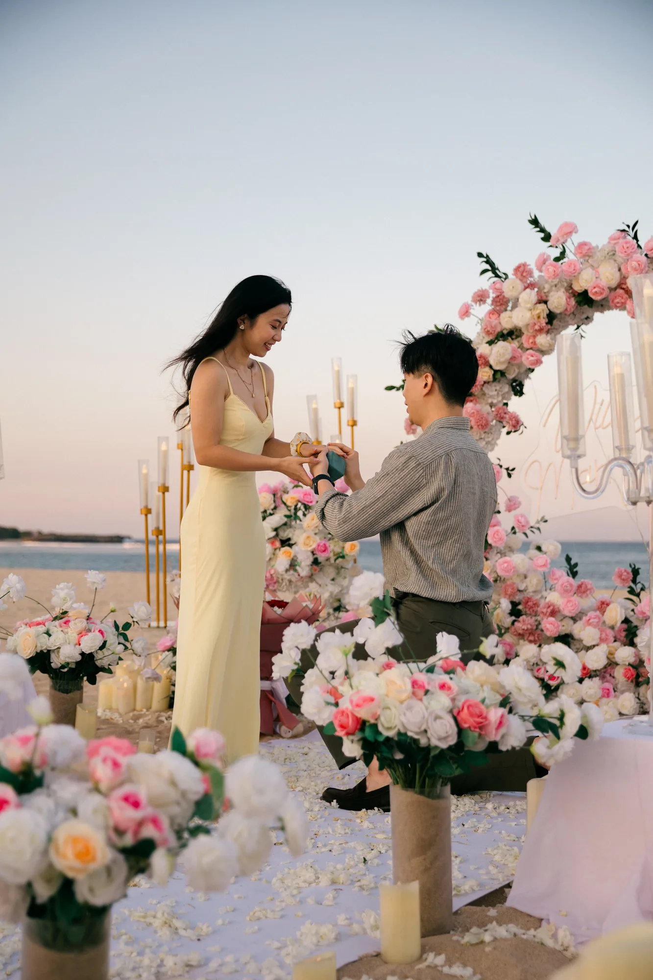 Couple embracing at their beach floral arch during a Bali proposal