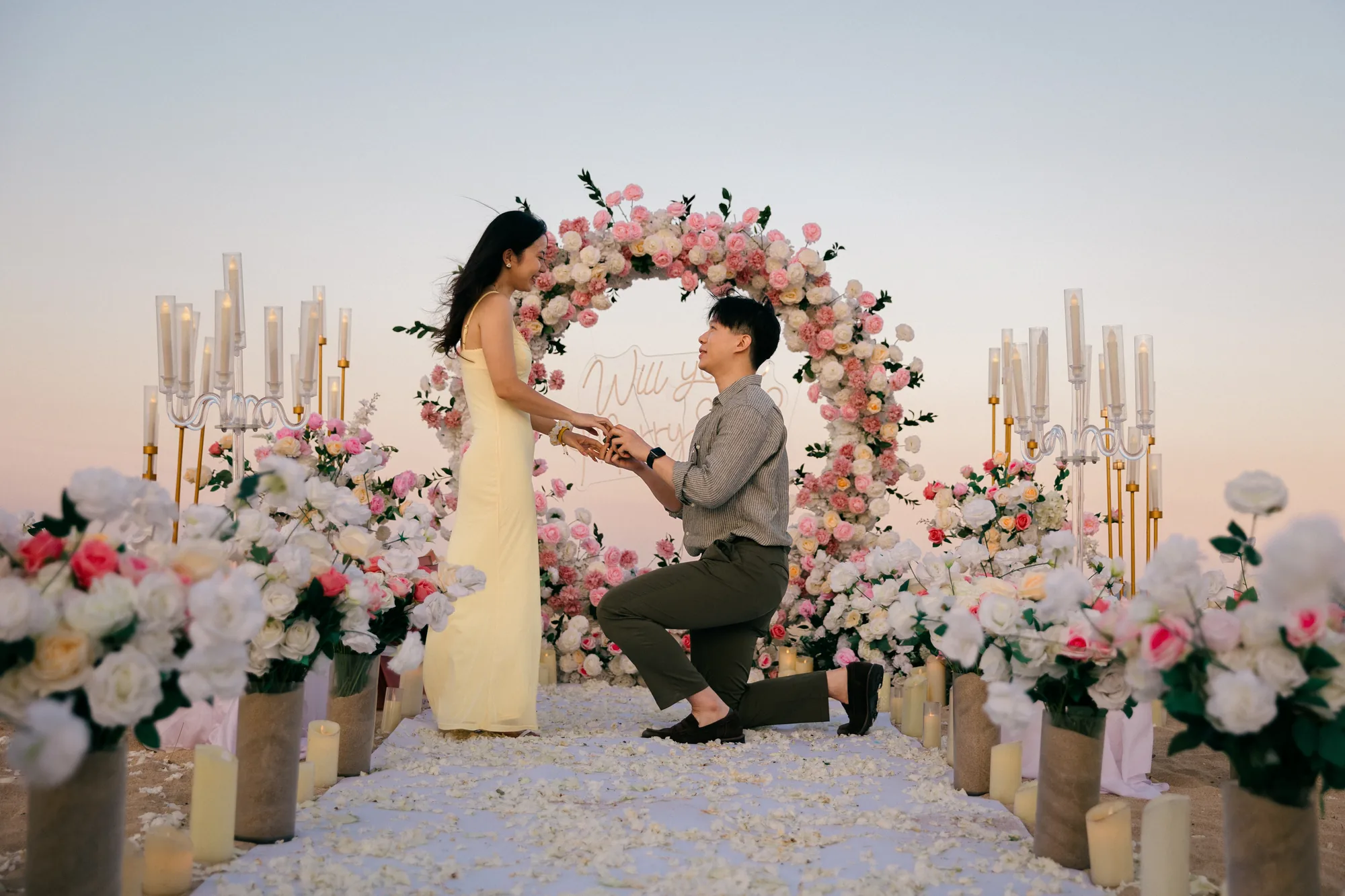 Man kneeling to propose at a floral arch on the beach at sunset in Bali