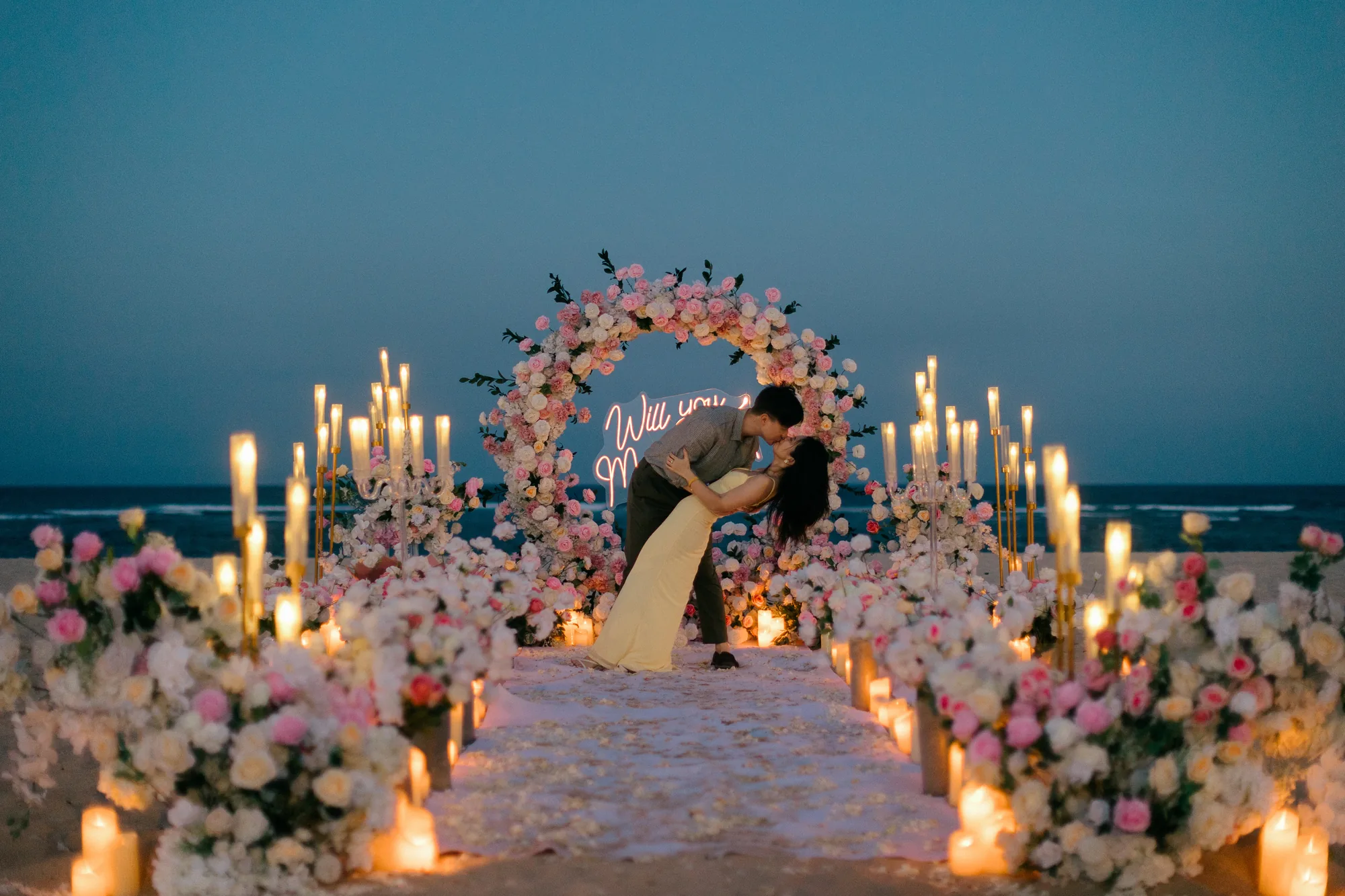 Couple kissing at a candlelit floral arch on the beach at night in Bali