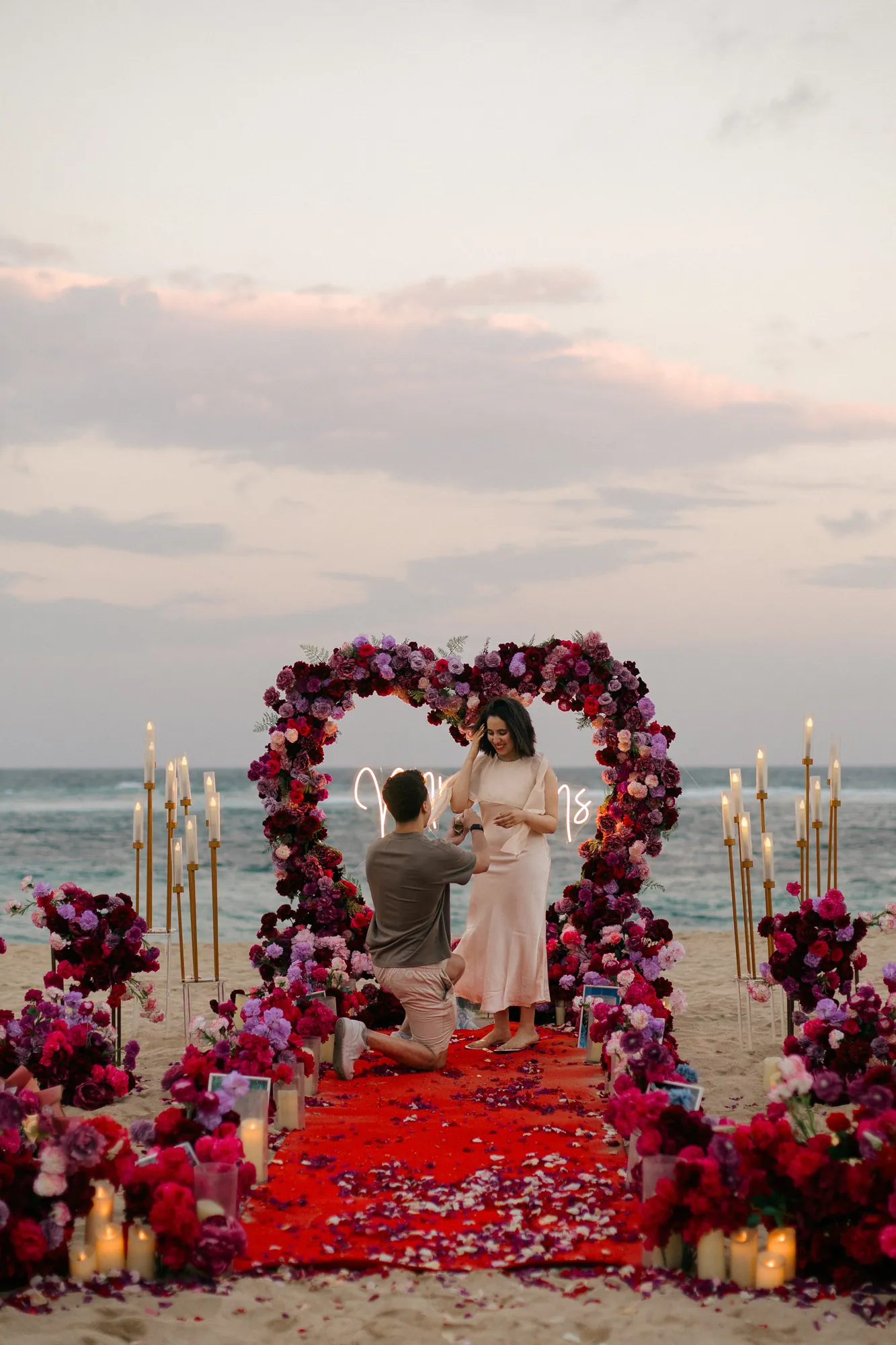 Man kneeling to propose at a red rose heart arch on a Bali beach