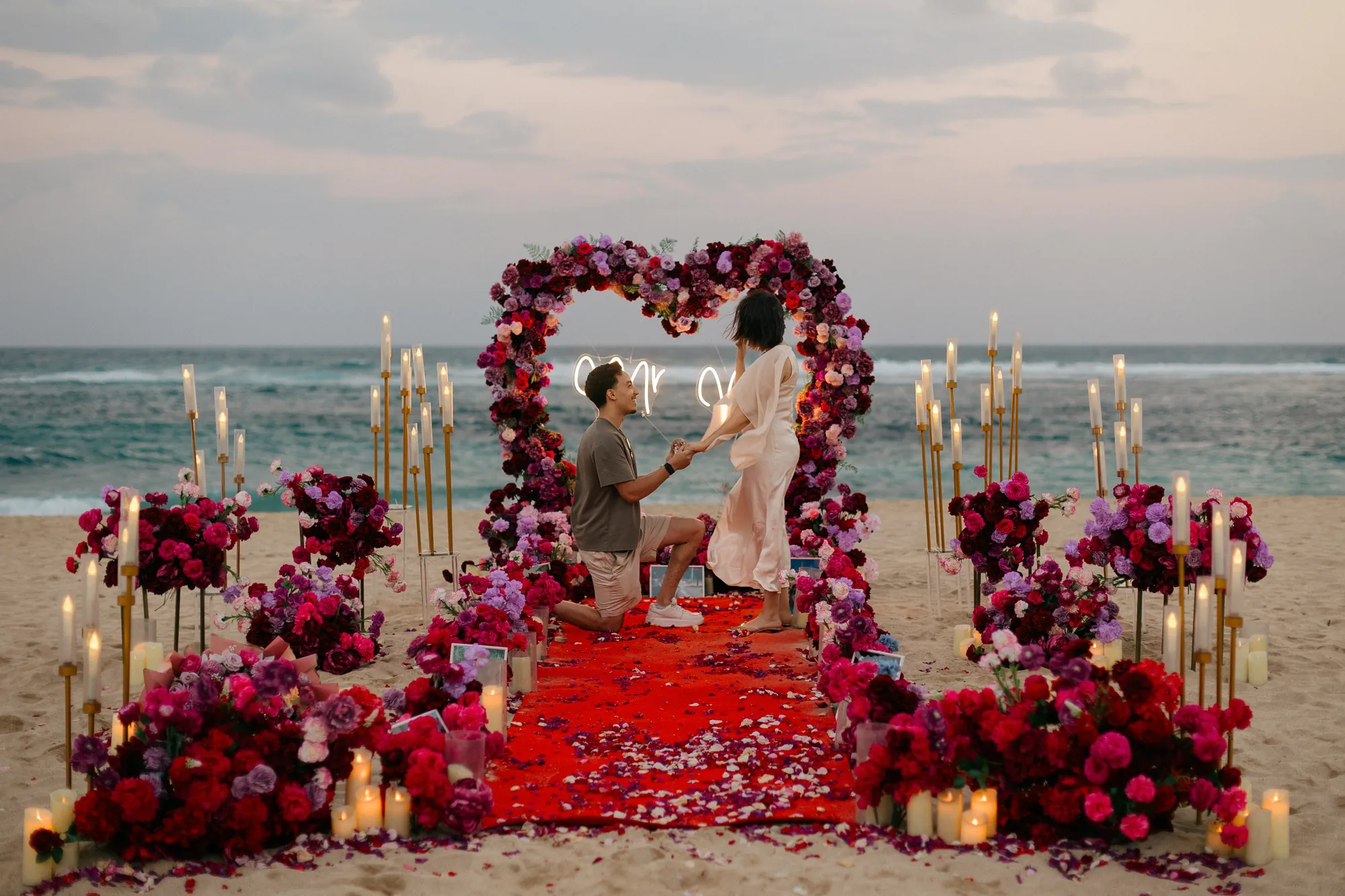 Beach proposal in Bali with a man kneeling at sunset by a rose heart arch