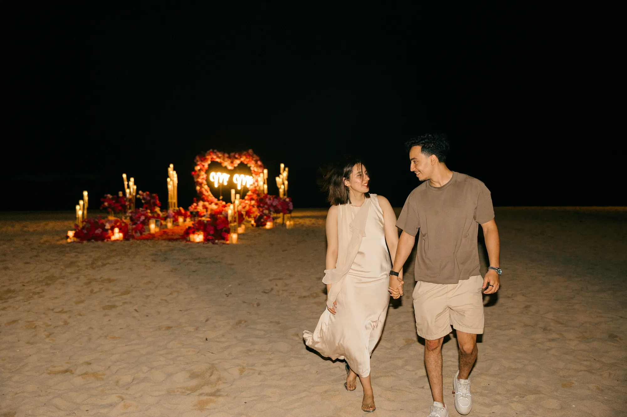 Couple walking hand in hand on a Bali beach at night after a proposal