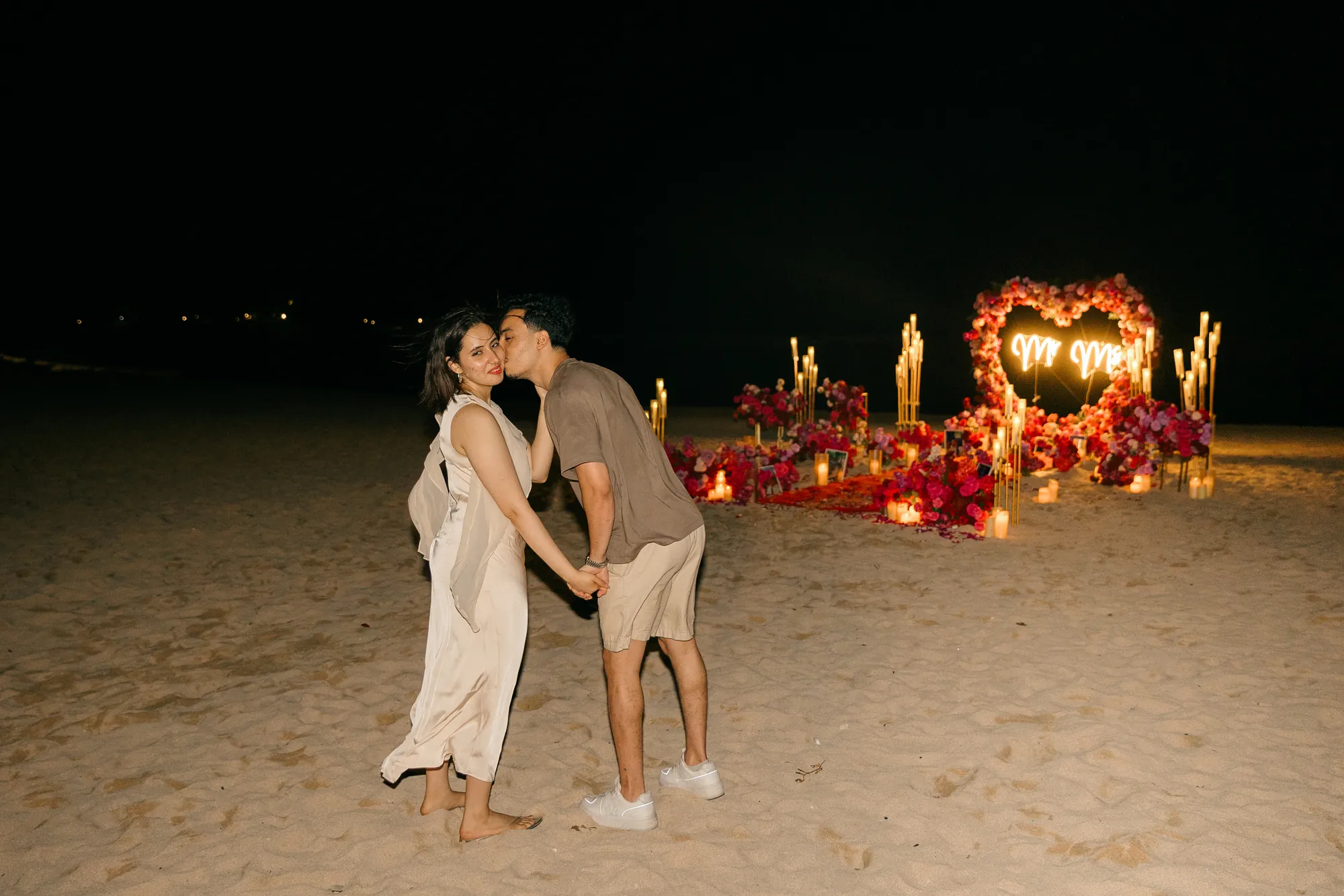 Couple kissing on a Bali beach at night beside a glowing heart arch