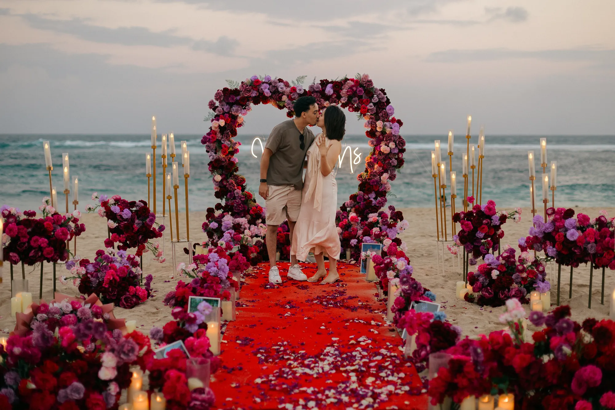 Couple at a red rose heart arch by the ocean at a Bali beach proposal