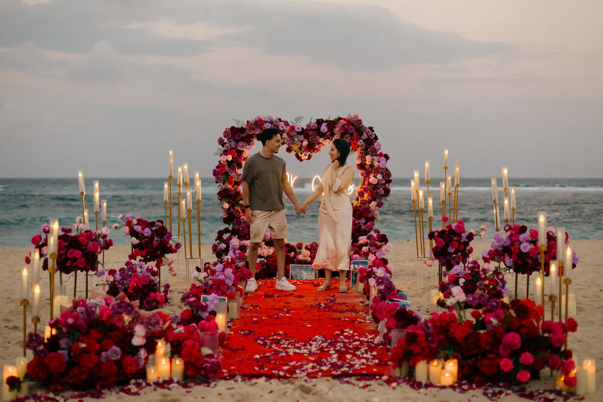 Couple embracing at a red rose heart arch during a Bali beach proposal