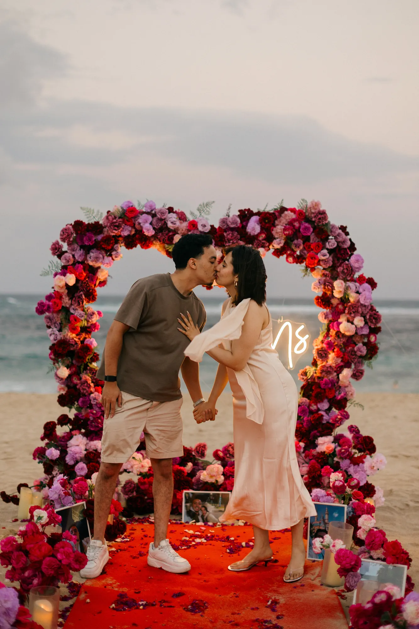 Couple kissing under a red rose heart arch at a Bali beach proposal