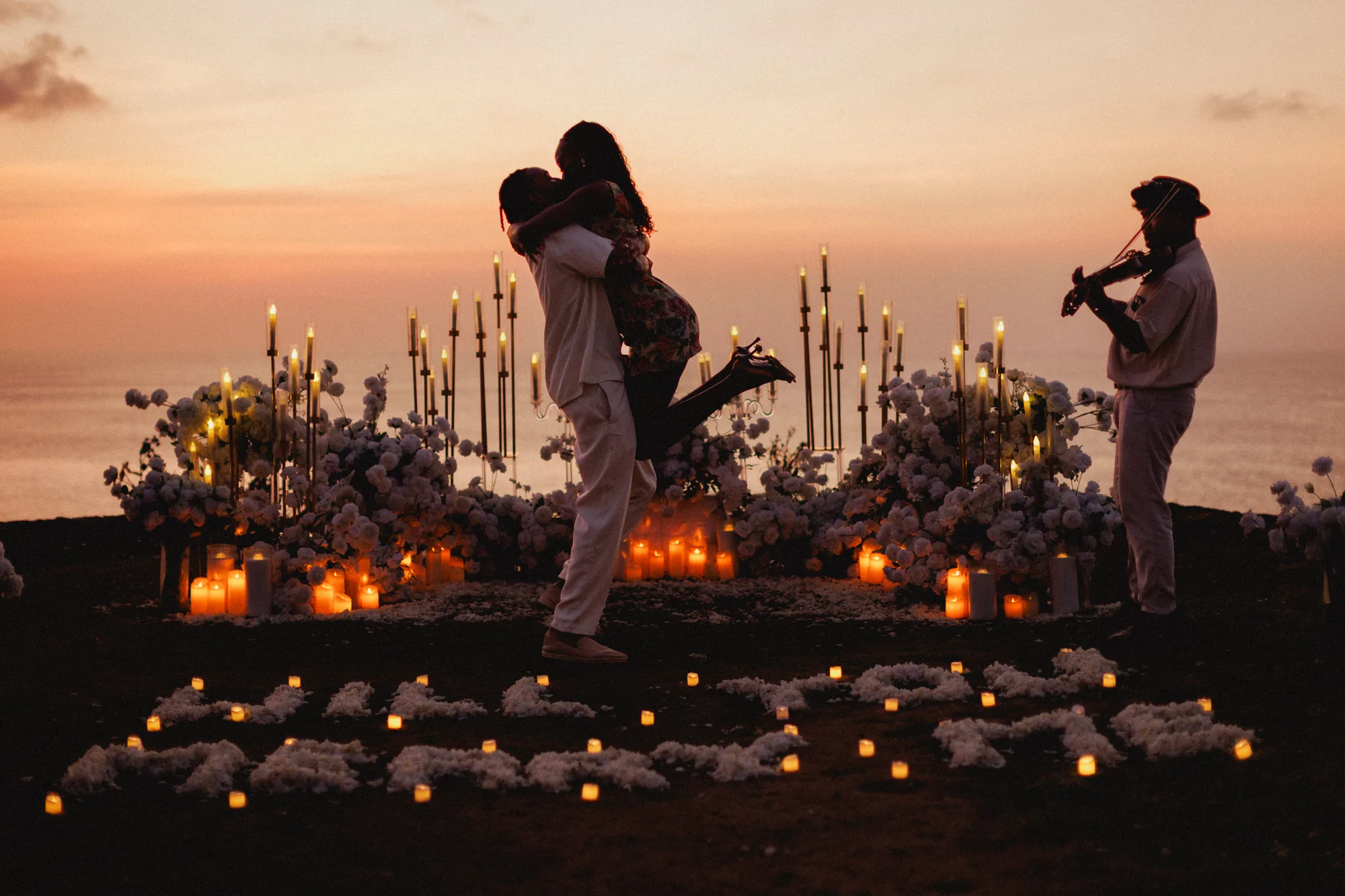 Man lifting his partner among candles at a Bali clifftop proposal