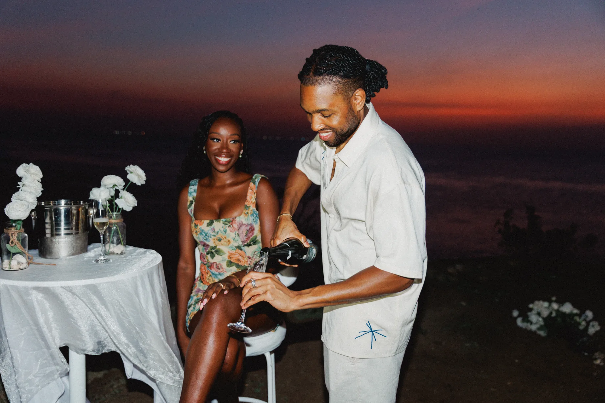 Couple opening champagne at a candlelit clifftop dinner in Bali