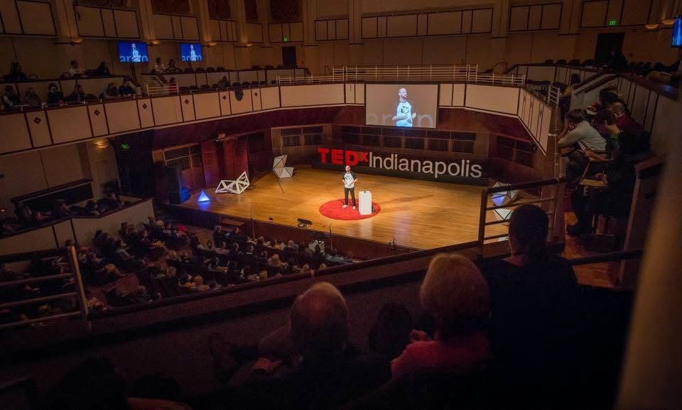 Ty Bush speaking on the TEDxIndianapolis stage, seen from the balcony