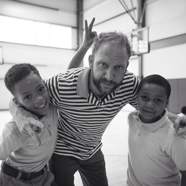 Ty poses with two smiling students in the gym