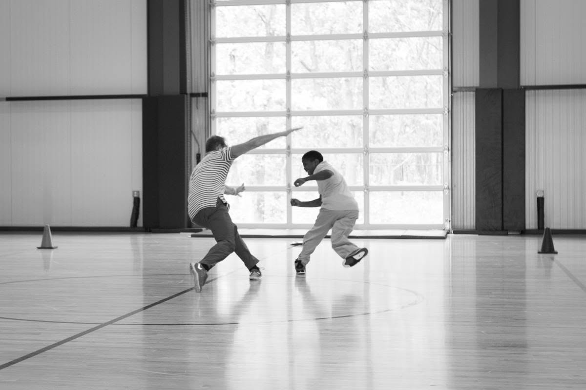 Ty and a student race across the court mid-stride while classmates cheer