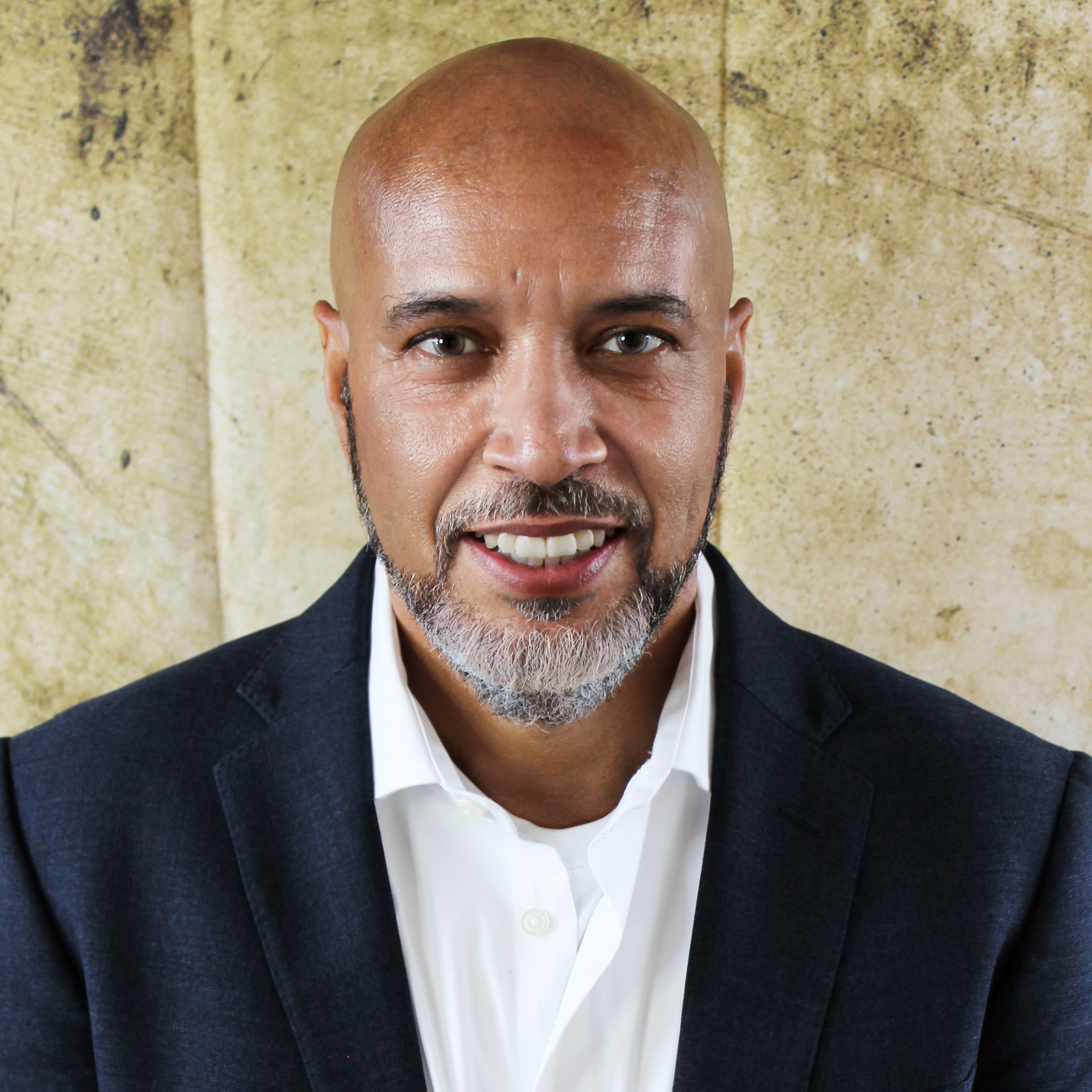 Smiling woman with short curly hair wearing large silver earrings and a light gray top.