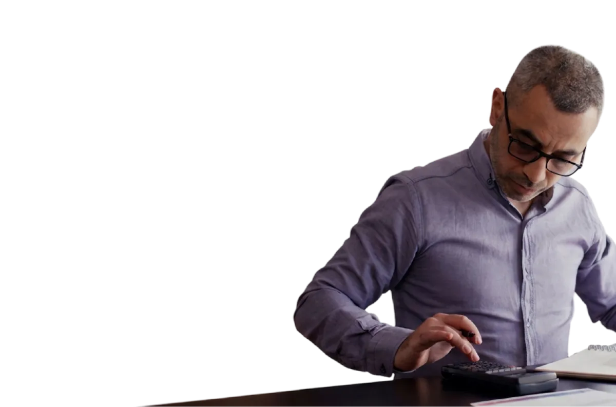 Man in glasses and a purple shirt using a calculator and checking documents on a desk.