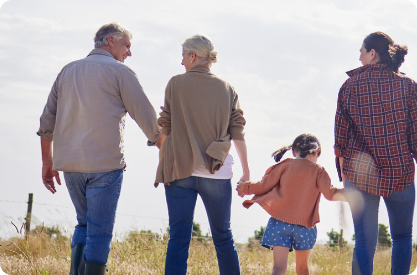 Two adults and a child walking hand in hand outdoors on a sunny day.