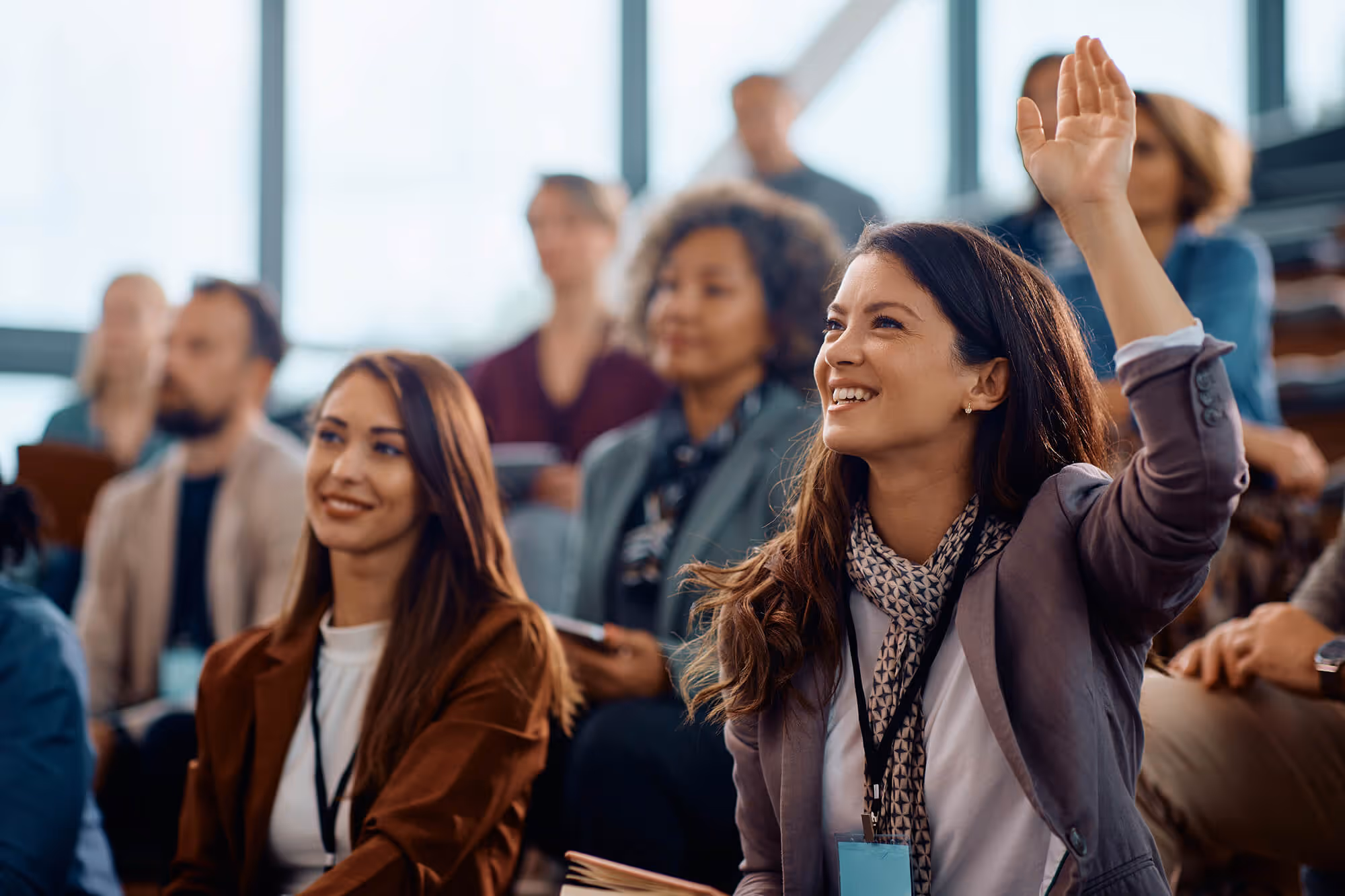 Smiling woman raising her hand during a group training session in a modern classroom.