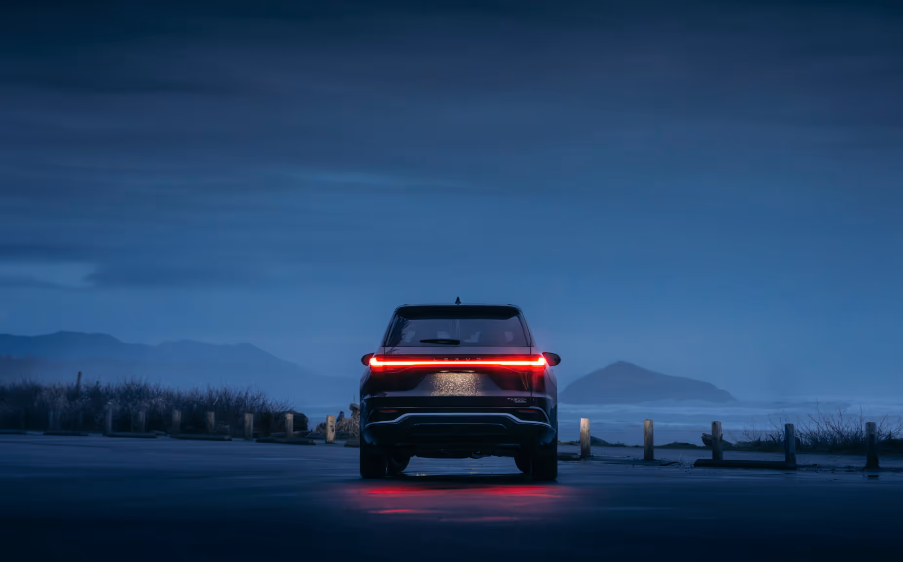 A promotional shot for Lexus showing the rear end on an SUV in the early evening overlooking the ocean with an island visible in the background.