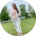 Smiling woman in white striped pants and top standing on grass with trees in background.