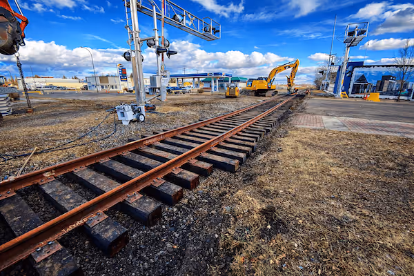 Railroad tracks under maintenance with excavator and construction workers near a railway crossing in a commercial area.