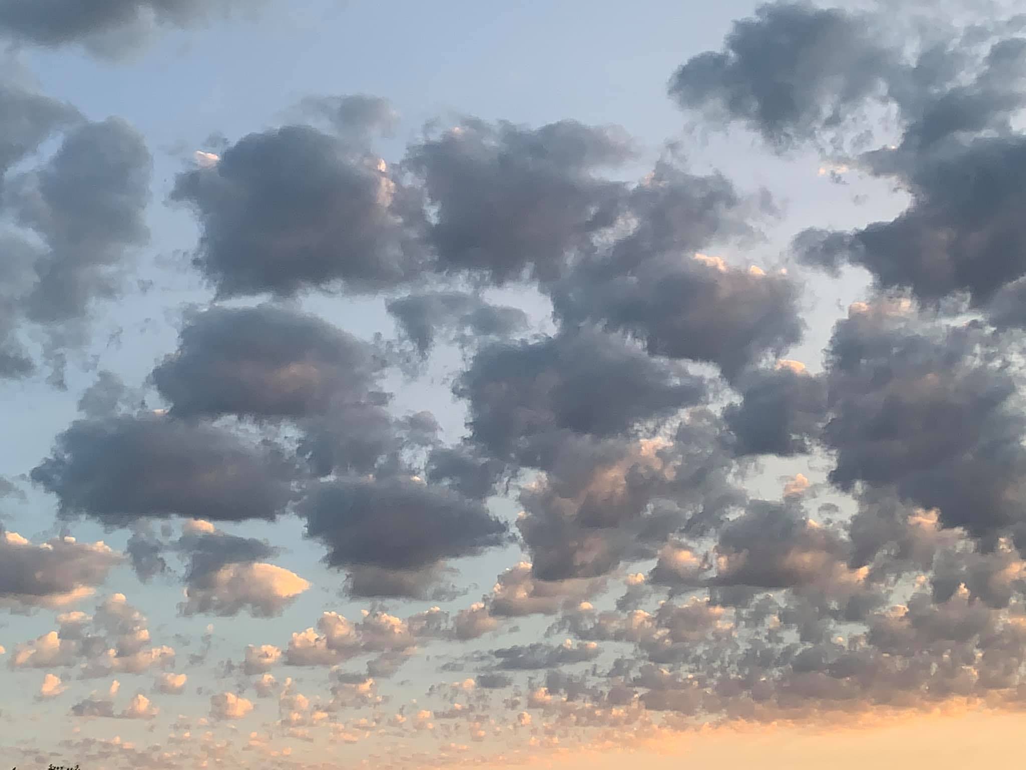 Sky filled with scattered dark clouds illuminated by soft sunlight during sunset.