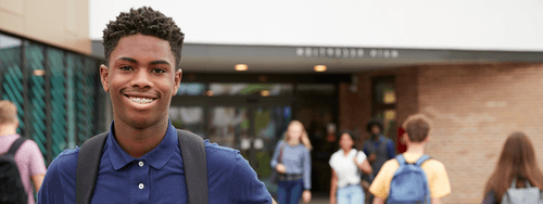 A student smiling, outside a school entrance