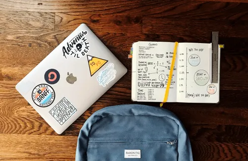 Bird's eye of a laptop, notepad, and bookbag positioned on a table.