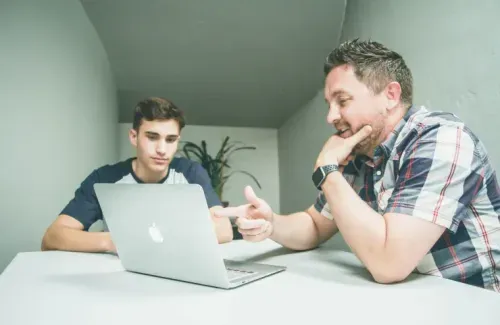 A man points at a laptop while a student listens