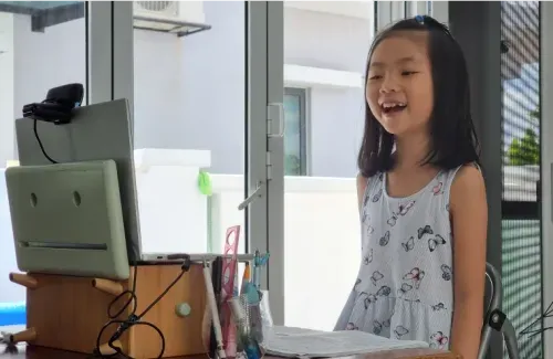 A young girl smiles at a laptop at a home desk