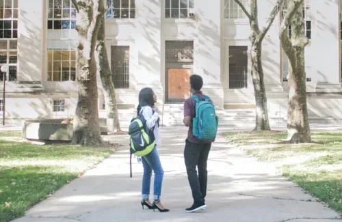 Two students stand talking in front of a school building