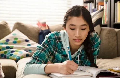A girl is lying down, studying and writing in her notebook
