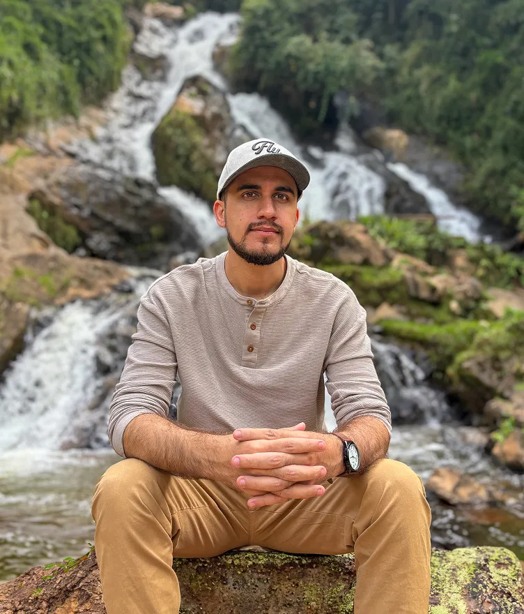 Juan Mac sitting outdoors in front of a waterfall, reflecting creativity and connection with nature